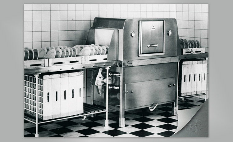 Historic commercial stainless steel dishwasher with dish racks and plates – early technology for efficient cleaning in restaurants and large kitchens.