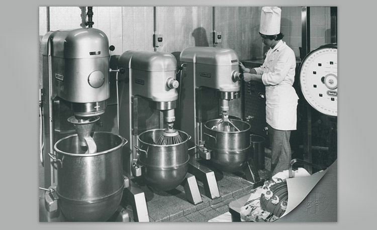 Historic image of a professional kitchen with three large Hobart mixers and a scale – early technology for efficient mixing and dough preparation.